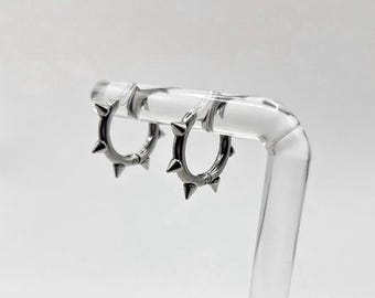 May include: A pair of silver hoop earrings with small spikes around the edge.