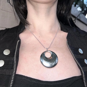 May include: A silver necklace with a large, round pendant. The pendant has a smooth, curved surface and a hole in the center.