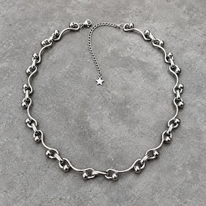 May include: A silver-toned metal chain necklace featuring a series of curved links connected by small spherical beads. The necklace includes an adjustable extender chain that terminates in a small, five-pointed star charm at the end of the clasp.
