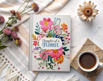 May include: A white book with a colorful embroidered floral design on the cover. The title of the book is "Thoughts of a Florist."