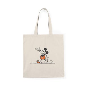 Könnte beinhalten: Eine beige Canvas-Tragetasche mit einem schwarzen Henkel und einem Schwarzweißbild von Mickey Mouse in seiner klassischen Pose, der eine rote Shorts trägt.