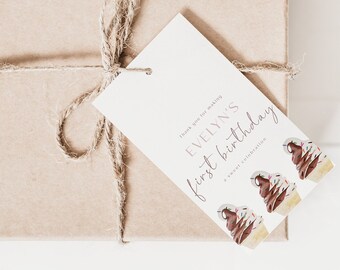 Puede incluir: Una caja de regalo marrón envuelta en cordel con una etiqueta de regalo blanca que dice "Evelyn's first birthday". La etiqueta tiene un gráfico de tres conos de helado con helado de chocolate y vainilla.