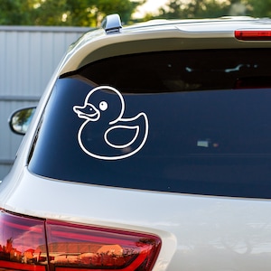 May include: A white rubber ducky decal on the back window of a silver car.