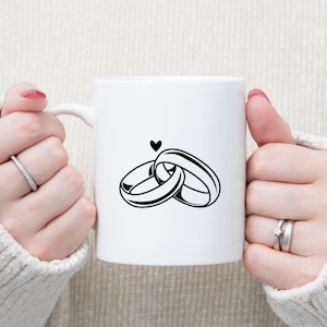 May include: White ceramic mug with a black graphic of two interlocking rings and a small heart above them.