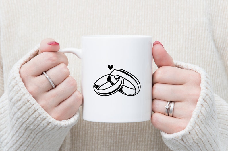 May include: White ceramic mug with a black graphic of two interlocking rings and a small heart above them.