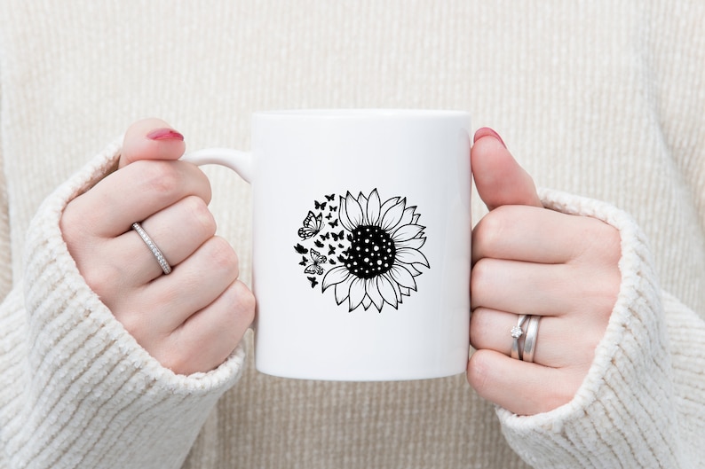 Puede incluir: Taza de cer&aacute;mica blanca con un dise&ntilde;o en blanco y negro de un girasol con mariposas que salen volando.