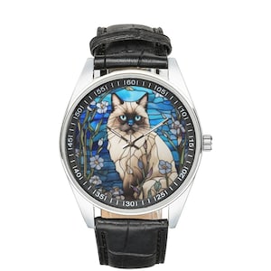 Op de afbeelding: Een zilveren polshorloge met een zwarte leren band heeft een kleurrijk glas-in-loodontwerp van een Siamese kat met blauwe ogen. De wijzerplaat van het horloge heeft Romeinse cijfers en een witte achtergrond.
