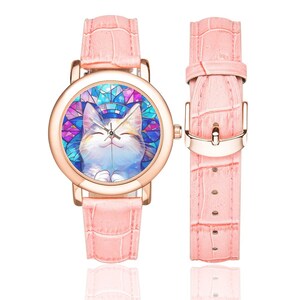 Op de afbeelding: Een roze leren polshorloge met een ros&eacute;gouden kast en een kleurrijk glas-in-loodontwerp met een lachende kat. Het horloge heeft een witte wijzerplaat met zwarte wijzers en zwarte cijfers.