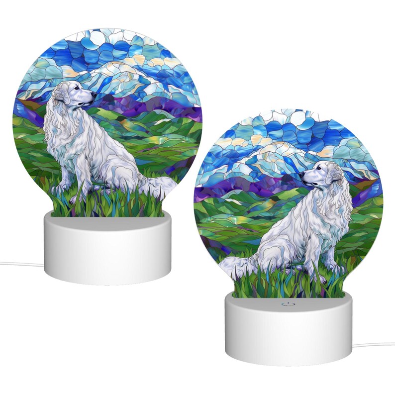 May include: Two white ceramic night lights with a stained glass design of a white dog sitting in a field with mountains in the background. The lights are illuminated and have a cord.