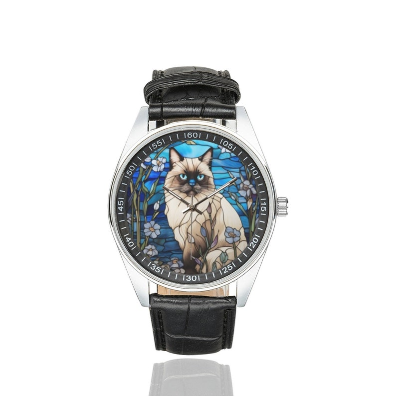 Op de afbeelding: Een zilveren polshorloge met een zwarte leren band heeft een kleurrijk glas-in-loodontwerp van een Siamese kat met blauwe ogen. De wijzerplaat van het horloge heeft Romeinse cijfers en een witte achtergrond.