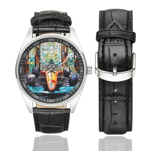 Puede incluir: Un reloj de pulsera de cuero negro con caja plateada y una esfera de estilo mosaico colorido que representa un coche de carreras. La esfera del reloj tiene n&uacute;meros alrededor del borde y una correa de cuero negro.