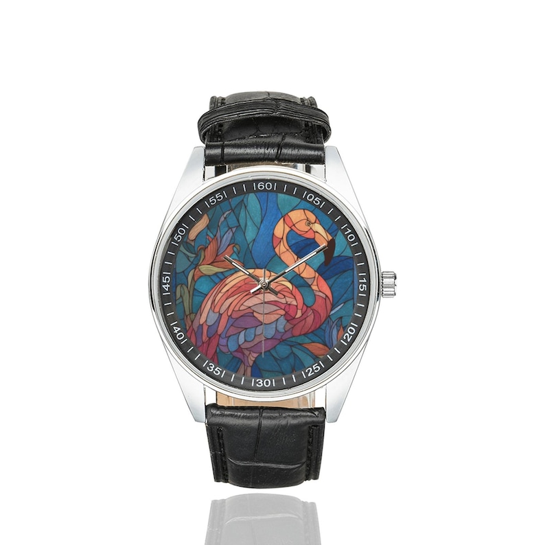 May include: A stainless steel wristwatch with a black leather band. The watch face features a colorful stained-glass design of a flamingo. The flamingo is depicted in shades of pink, orange, and purple against a blue background.