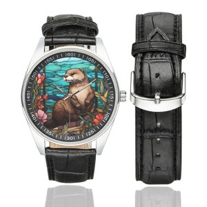 May include: A silver wristwatch with a black leather band. The watch face features a stained glass design of an otter in a blue and green water scene. The numbers on the watch face are in black.