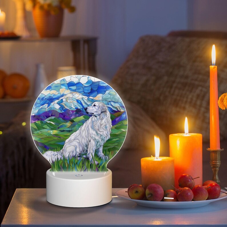 May include: A white dog with a stained glass design sits in a field with mountains in the background. The dog is illuminated by a light that shines through the stained glass design. The light is on a white base.