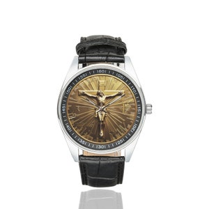 May include: A silver wristwatch with a black leather band. The watch face features a gold-toned image of Jesus Christ on the cross with a sunburst design.