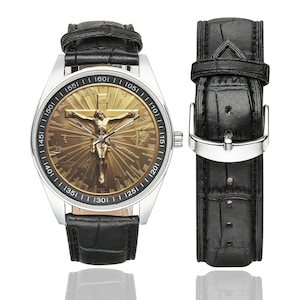 May include: A black leather wristwatch with a silver face and a gold-toned image of Jesus Christ on the cross. The watch face has numbers around the edge and a black leather band.
