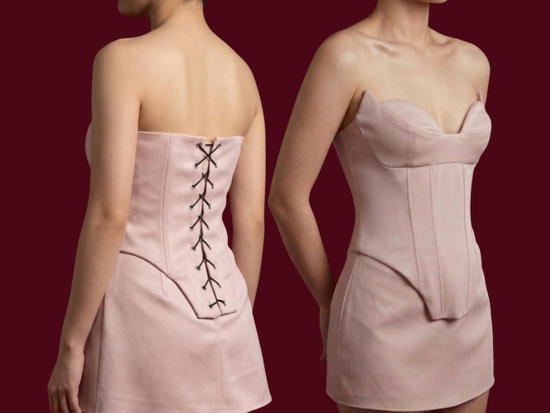May include: A light pink strapless corset dress. The dress features a structured bodice with vertical seams and a mini skirt. The back of the dress has a lace-up closure with black lacing. The dress is shown from the front and back.