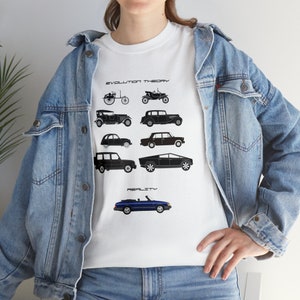 Puede incluir: Camiseta blanca con una ilustración en blanco y negro de la evolución de los coches. La ilustración muestra una progresión de diseños de coches desde un carruaje tirado por caballos hasta un coche moderno. El texto "EVOLUTION THEORY" y "REALITY" está impreso en la camiseta.