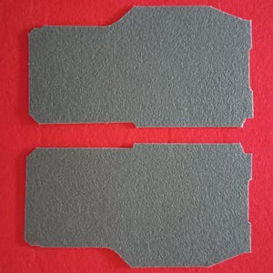 May include: Two grey felt pads, each with a slightly different shape, are shown against a red background.