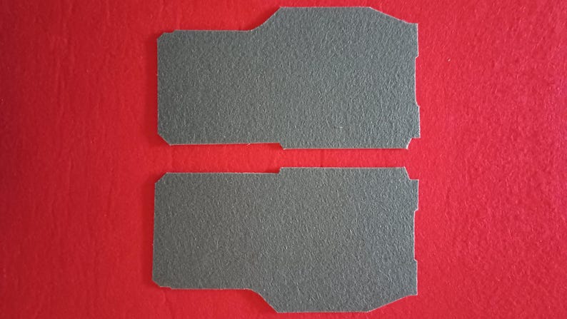May include: Two grey felt pads, each with a slightly different shape, are shown against a red background.