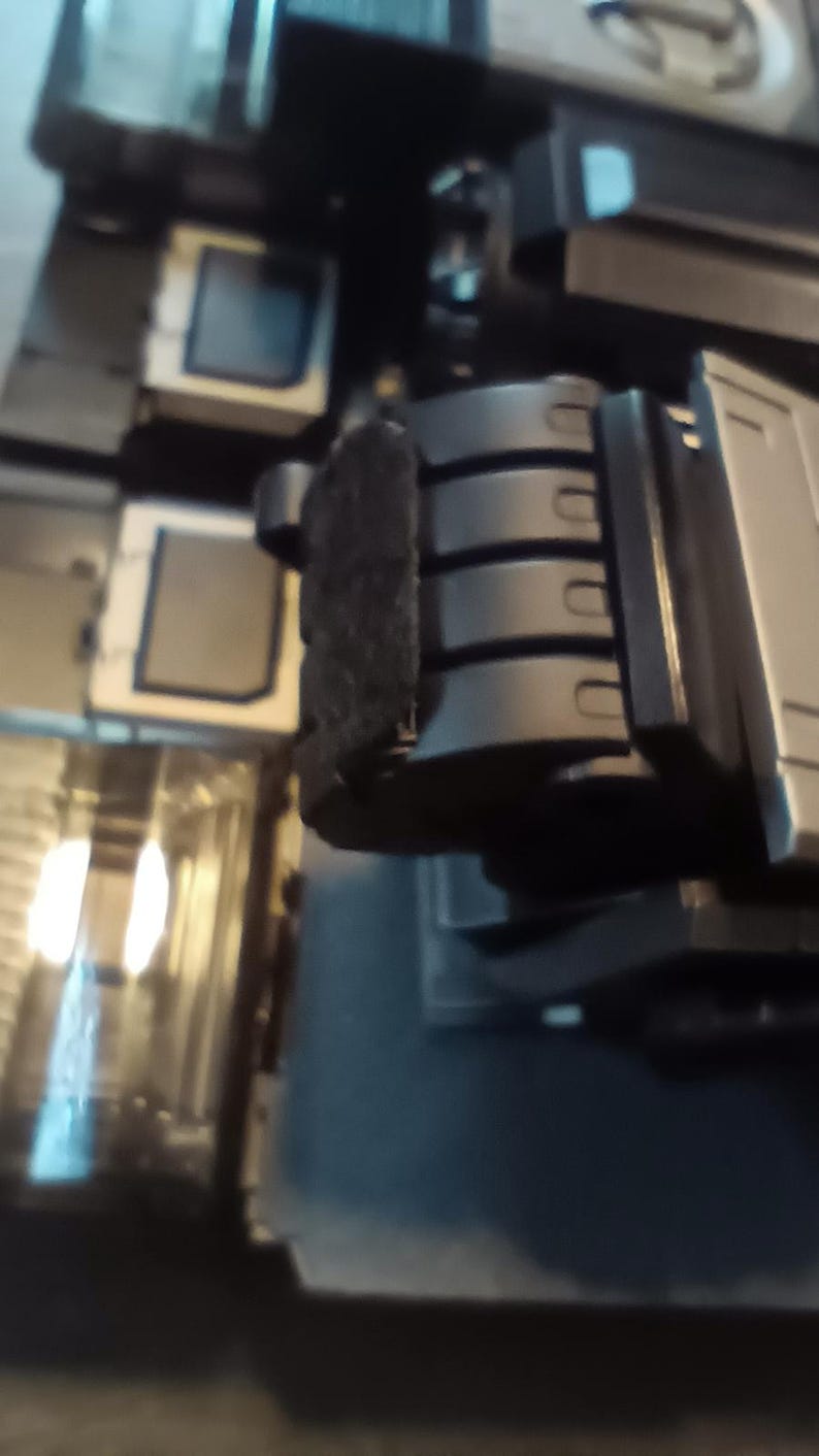 May include: Close-up of a black robotic hand with four fingers. The hand is made of metal and has a textured surface. The hand is attached to a larger robotic arm.