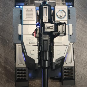 May include: A black and silver toy tank with a long black barrel and blue lights. The tank has a detailed design with multiple panels and compartments.