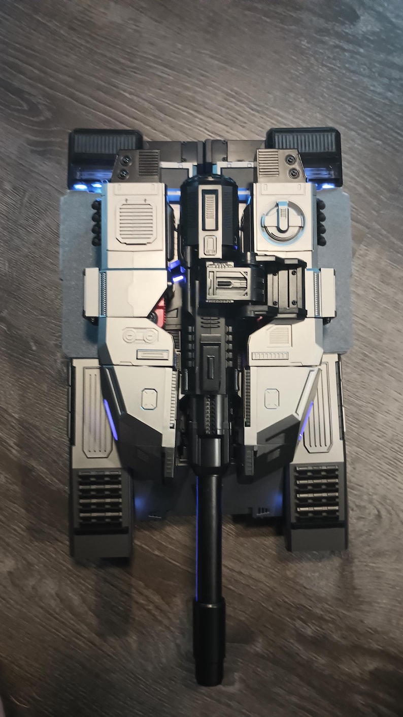 May include: A black and silver toy tank with a long black barrel and blue lights. The tank has a detailed design with multiple panels and compartments.