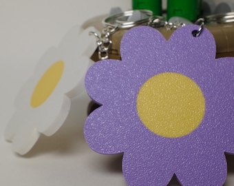 Peut inclure: Porte-clés en forme de fleur violet avec un centre jaune. Le porte-clés est fait d'un matériau texturé et a un anneau de clé argenté.