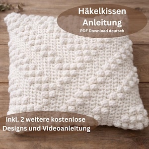 May include: A square, cream-coloured crochet cushion with a textured, raised pattern. The cushion is on a wooden surface. Text on the image reads "Häkelkissen Anleitung PDF Download deutsch" and "inkl. 2 weitere kostenlose Designs und Videoanleitung."