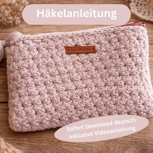 Può includere: Un astuccio all'uncinetto rosa chiaro con chiusura a zip e nappa. L'astuccio presenta un motivo a stella strutturato e una piccola etichetta in pelle marrone con la scritta "Handmade". Il testo "Häkelanleitung" è in alto.