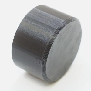 May include: A black plastic cap with a ridged surface. The cap is round and has a flat top.