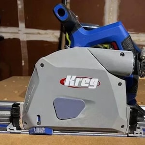 May include: A gray and blue Kreg brand circular saw with a blue handle and a black power cord. The saw is mounted on a track system.