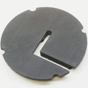 May include: A black plastic disc with a cut-out section in the shape of a right angle. The disc has a textured surface.