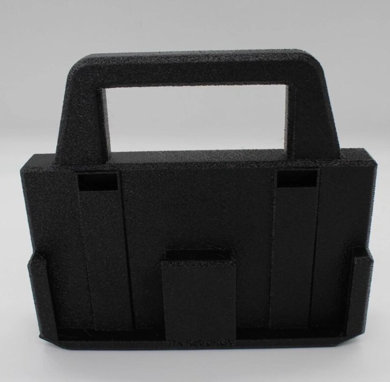 May include: A black, textured, 3D-printed carrying case with a handle. The case has a rectangular opening in the handle and a slot on the front. The case is designed to hold a small object.