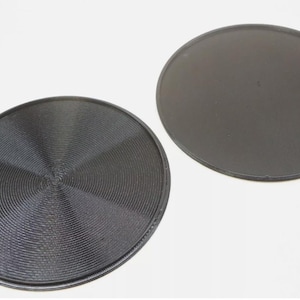 May include: Two black round trays, one with a smooth surface and the other with a textured, concentric circle pattern.