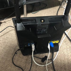 May include: A black router with two antennas, a power cord, and two ethernet cables connected to the back. The router has a label that says "ASUS" and has a warning label with text in multiple languages.