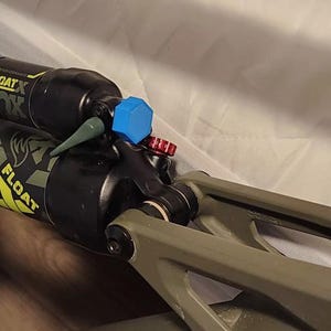 May include: A close-up of a black and green mountain bike shock absorber with a blue and red cap. The shock absorber is labeled "FLOAT" and "FOX".