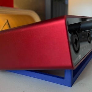 May include: A red audio interface with two knobs and two input jacks. The interface is sitting on a blue stand.