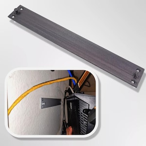 May include: A black metal cable management strip with four screw holes. The strip is mounted to a wall and has a yellow cable running along it.