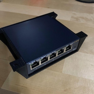 May include: A black 6-port Gigabit desktop switch with a black plastic enclosure. The switch has a label that reads "tp-link 6-port Gigabit Desktop Switch".