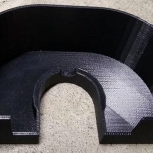 May include: A black, semi-circular 3D-printed object with a curved top and a central archway. The object has a textured surface and appears to be made of a solid material. The design suggests a structural or functional component.