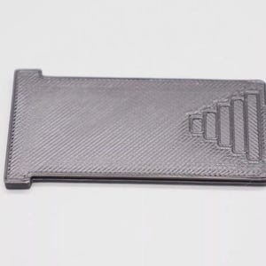 May include: A gray plastic 3D printed object with a geometric design. The object has a rectangular shape with a small tab on the side.