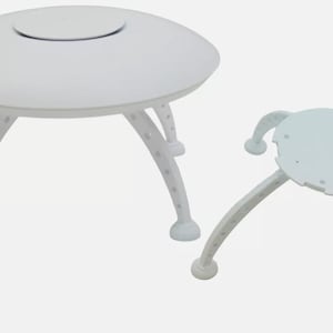 May include: Two white plastic UFO-shaped tables with three legs each. The larger table has a round top with a small circular opening in the center. The smaller table has a flat top.