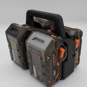 May include: A black and orange power tool battery holder with a black handle. The holder contains three 18V Lithium Ion batteries. The batteries are black and gray with orange accents.