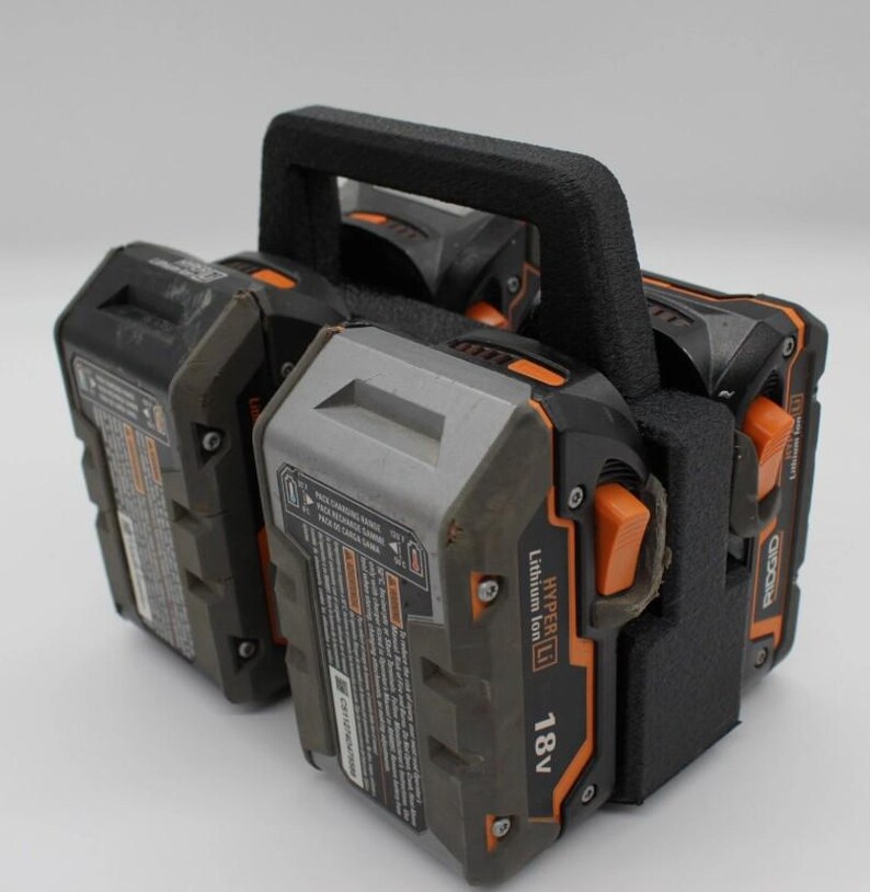 May include: A black and orange power tool battery holder with a black handle. The holder contains three 18V Lithium Ion batteries. The batteries are black and gray with orange accents.