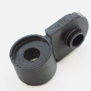 May include: Black plastic 3D printed part with a round hole and a smaller round hole on the side.