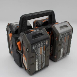 May include: A black and orange power tool battery holder with a textured handle. The holder contains multiple black and gray 18V batteries with orange accents. The batteries have printed labels and are designed for power tools.