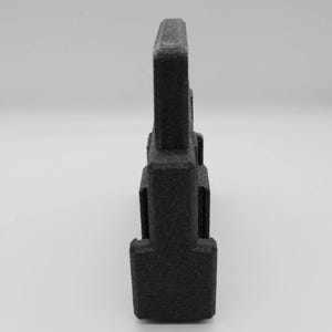 May include: A black, 3D-printed object with a rectangular shape and a textured surface. The object has a vertical, tower-like design with a series of stacked rectangular sections. The top section is wider than the base.