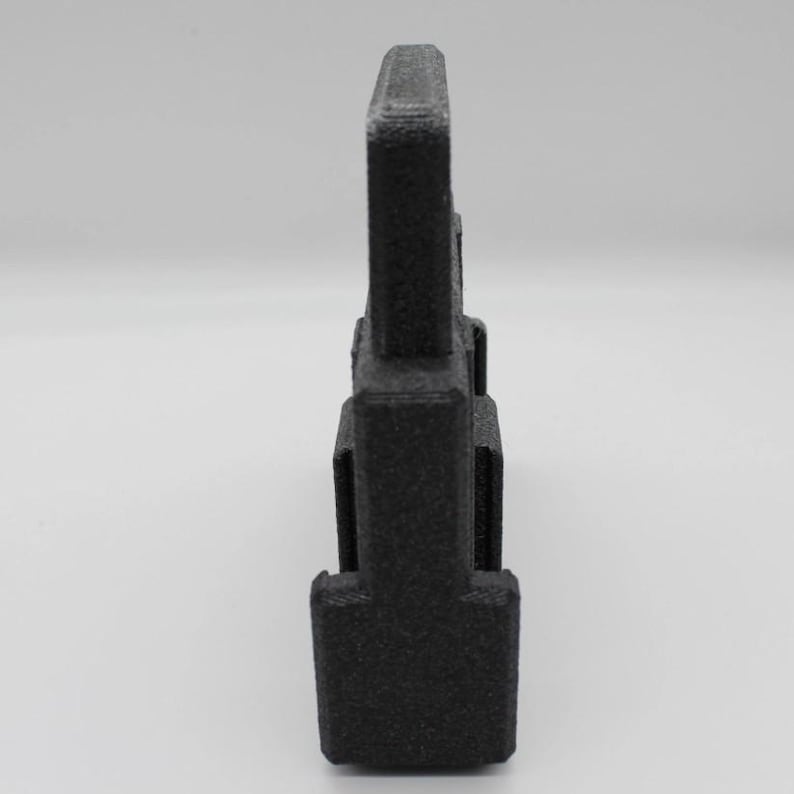 May include: A black, 3D-printed object with a rectangular shape and a textured surface. The object has a vertical, tower-like design with a series of stacked rectangular sections. The top section is wider than the base.
