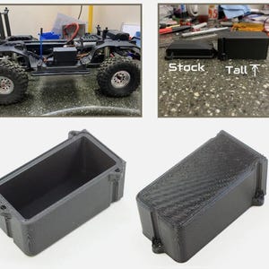 May include: Two 3D printed battery boxes for a remote control car. The box on the left is labeled "Stock" and the box on the right is labeled "Tall".